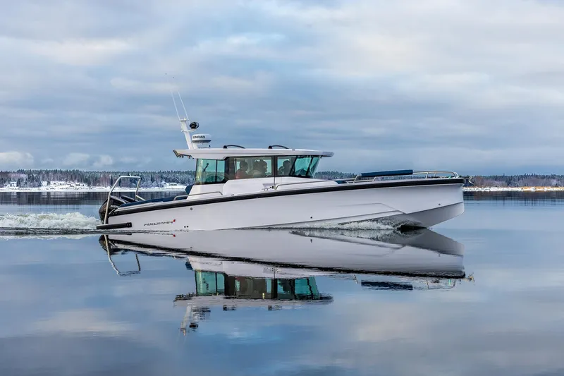 Slide: The Image of 2025 Axopar 29 Cross Cabin boat on calm water, reflecting sky and shoreline. - 1