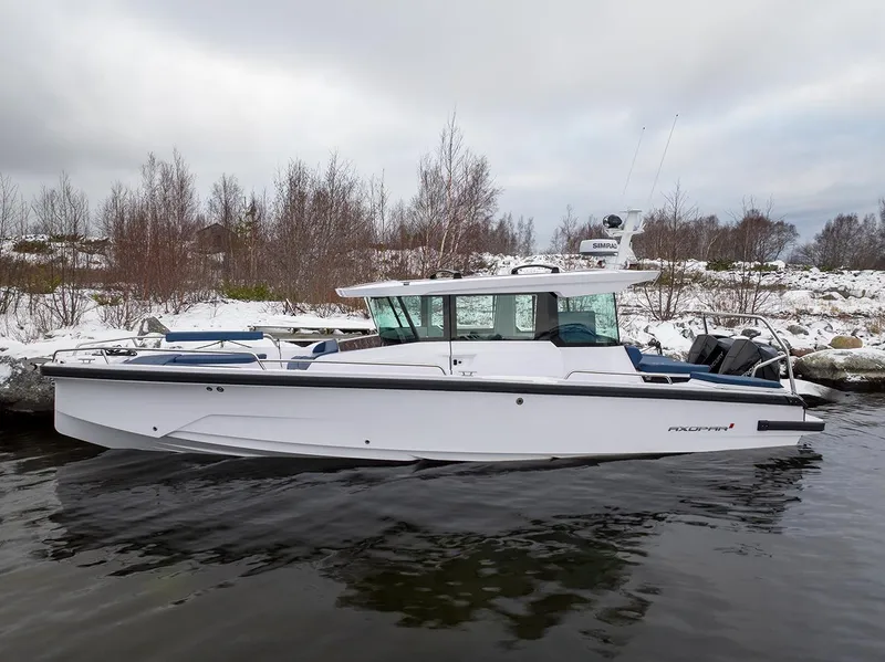 Slide: The Image of 2025 Axopar 29 Cross Cabin boat on a snowy shoreline, sleek design, winter setting. - 2