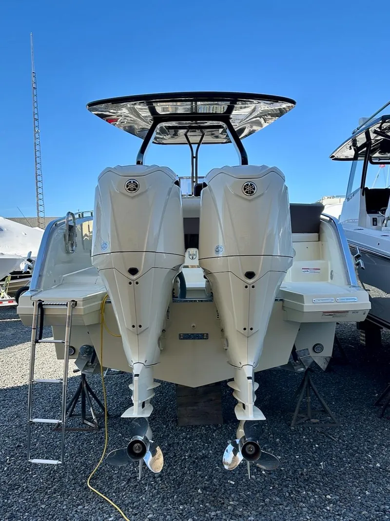 Slide: The Image of 2024 Invictus GT320S boat with dual outboard motors, rear view, parked on gravel. - 2