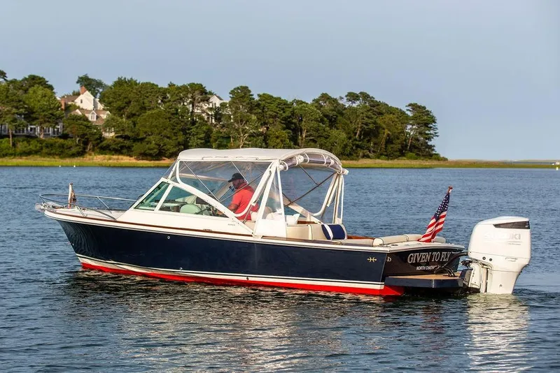 Slide: The Image of 2021 Hunt Yachts Harrier 26 cruising on a serene lake with lush green shoreline. - 56