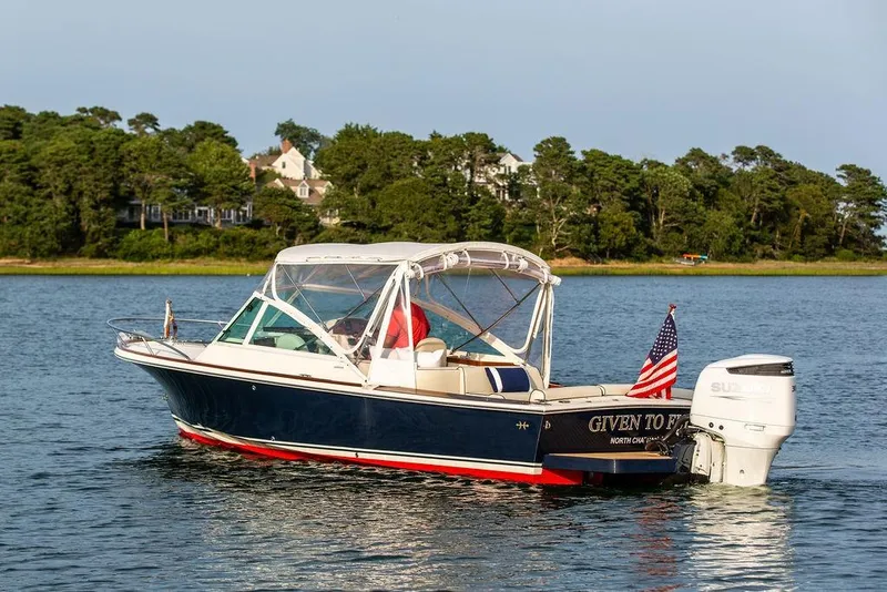 Slide: The Image of 2021 Hunt Yachts Harrier 26 cruising on a serene lake with lush green shoreline. - 58