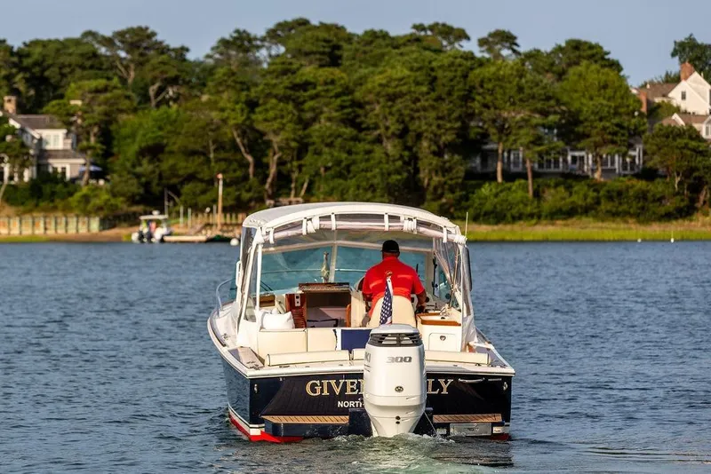 Slide: The Image of 2021 Hunt Yachts Harrier 26 cruising on a serene lake with lush greenery in the background. - 60