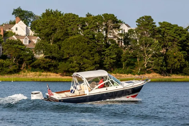 Slide: The Image of 2021 Hunt Yachts Harrier 26 cruising on a scenic lake with houses in the background. - 63