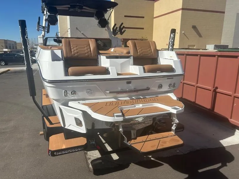 Slide: The Image of 2025 Malibu 26 LSV boat with tan seating and swim platform, parked outdoors. - 9