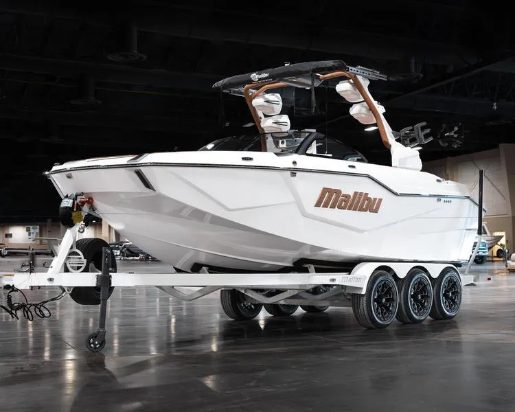 Slide: The Image of 2025 Malibu M230 boat on trailer in indoor showroom setting. - 2