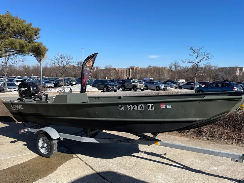 Slide: The Image of 2021 Lowe 1648 Jon boat on trailer in parking lot, clear sky background. - 1