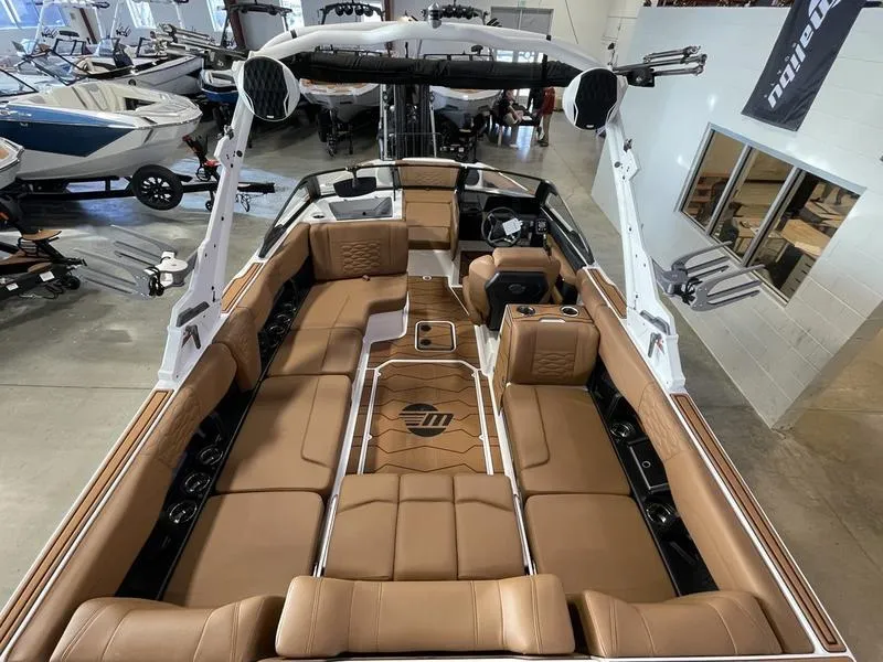 Slide: The Image of 2025 Malibu 24 MXZ boat interior with luxurious brown seating in a showroom. - 13