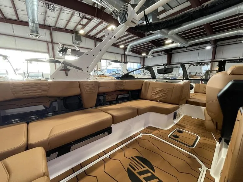 Slide: The Image of 2025 Malibu 24 MXZ boat interior with luxurious tan seating in a showroom. - 14