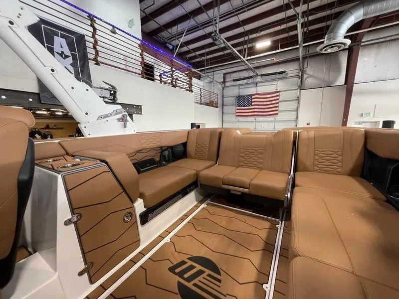 Slide: The Image of 2025 Malibu 24 MXZ boat interior with brown leather seating in a showroom. - 17