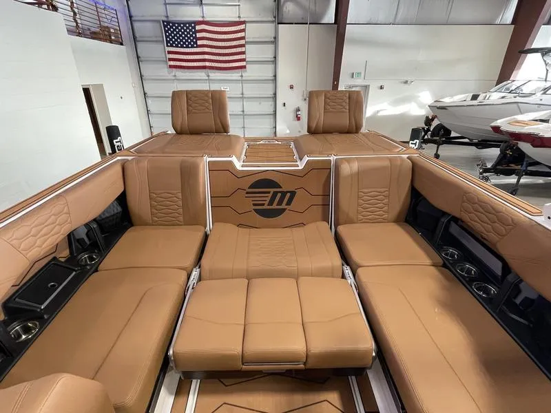 Slide: The Image of 2025 Malibu 24 MXZ boat interior with tan leather seating, American flag in background. - 23