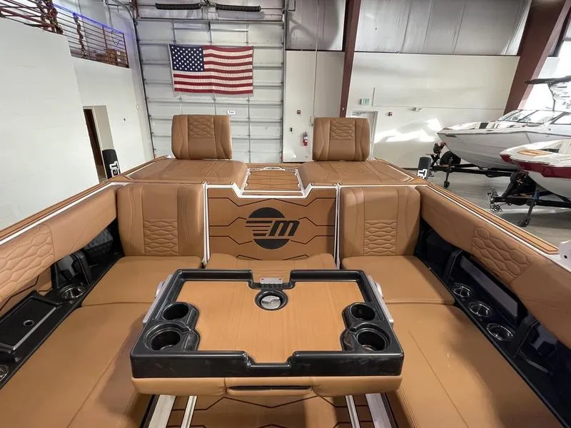 Slide: The Image of 2025 Malibu 24 MXZ boat interior with tan seating and cup holders in a showroom. - 24