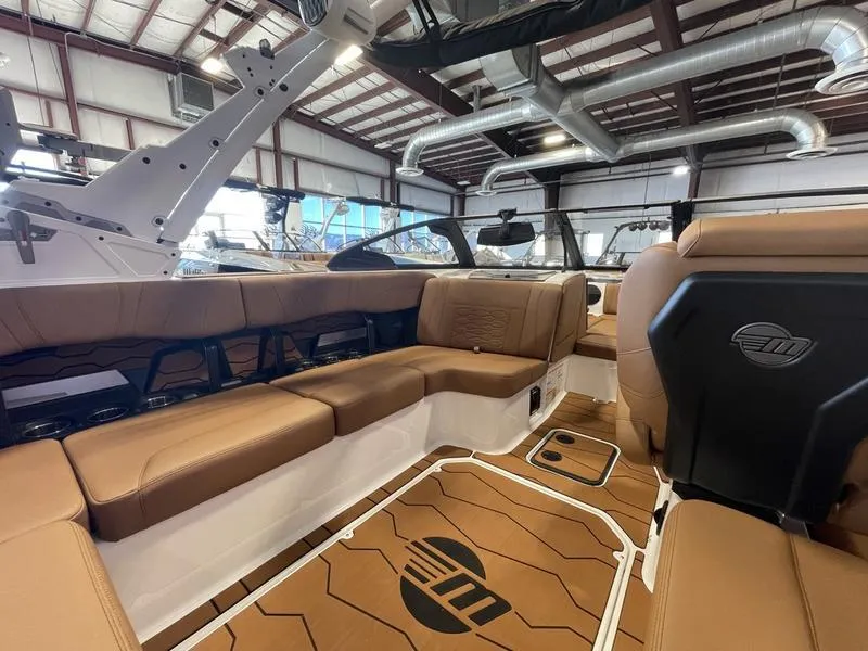 Slide: The Image of 2025 Malibu 22 MXZ boat interior with brown leather seating in a warehouse setting. - 11