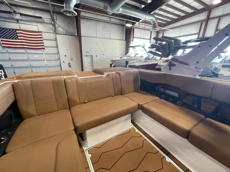 Slide: The Image of 2025 Malibu 22 MXZ boat interior with tan seating in a warehouse setting. - 16