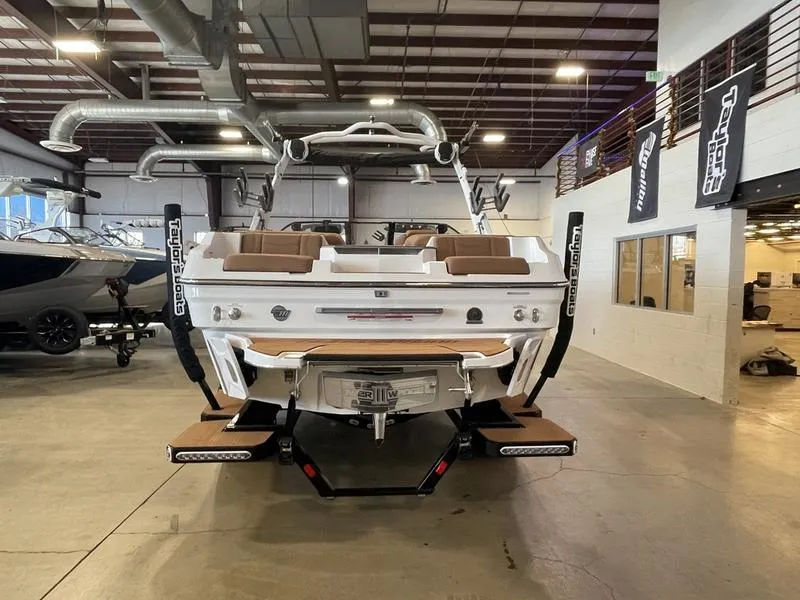 Slide: The Image of 2025 Malibu 22 MXZ boat in showroom, rear view with wakeboard racks and swim platform. - 8