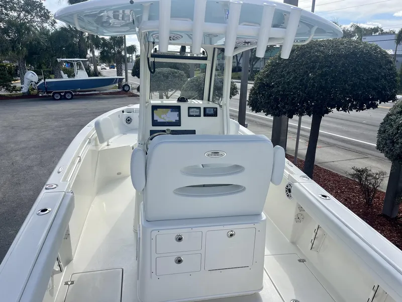 Slide: The Image of 2025 Cobia 240 CC boat interior with helm and seating, parked near trees. - 11
