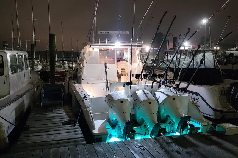 Slide: The Image of 2019 Pursuit OS 355 Offshore boat docked at night with illuminated engines. - 11