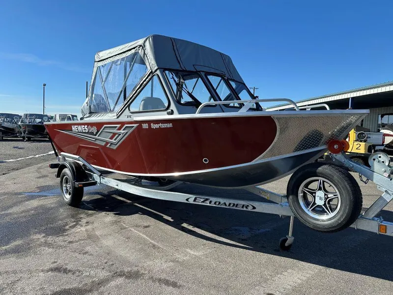 The Image of 2025 Hewescraft 180 Sportsman boat on trailer, red exterior, parked outdoors. - 0