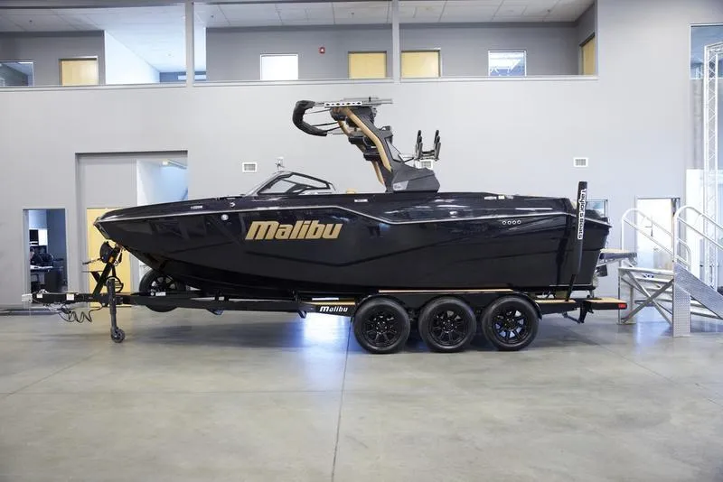 Slide: The Image of 2025 Malibu M242 boat on trailer in indoor showroom. - 1