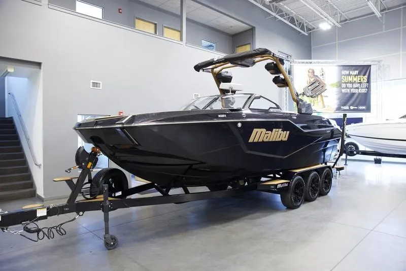 Slide: The Image of 2025 Malibu M242 boat on trailer in showroom, sleek black design. - 2