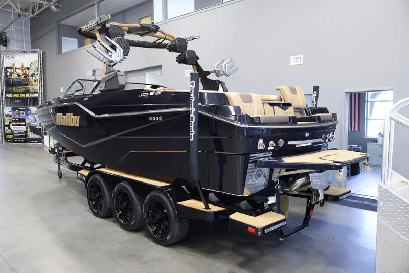 Slide: The Image of 2025 Malibu M242 boat on trailer in showroom, featuring sleek black design and modern amenities. - 3