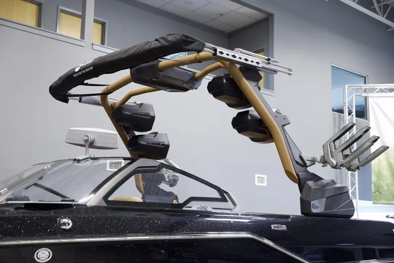 Slide: The Image of 2025 Malibu M242 boat with advanced wakeboard tower and sleek design in showroom setting. - 6