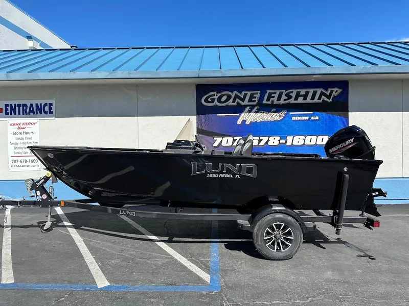 Slide: The Image of 2025 Lund 1650 Rebel XL SS boat on trailer, parked outside dealership. - 0