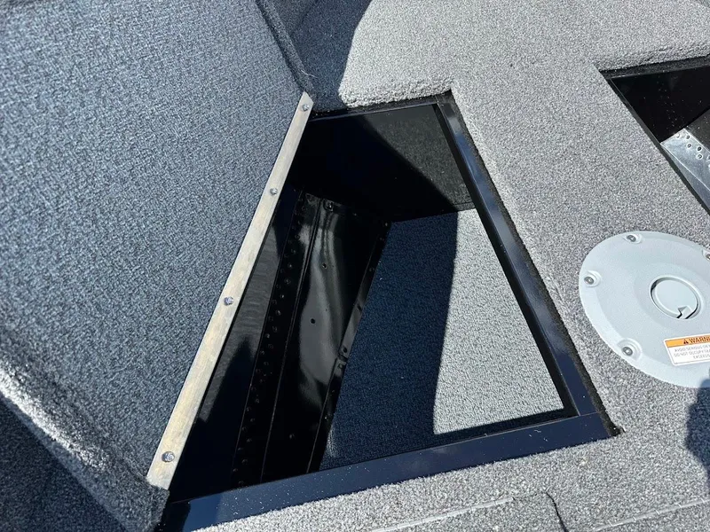 Slide: The Image of 2025 Lund 1650 Rebel XL SS boat storage compartment with gray carpeted interior. - 23