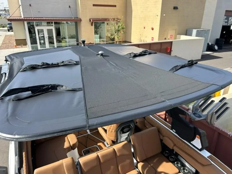 Slide: The Image of 2025 Malibu M230 boat with a sleek black cover and tan interior, parked outdoors. - 25