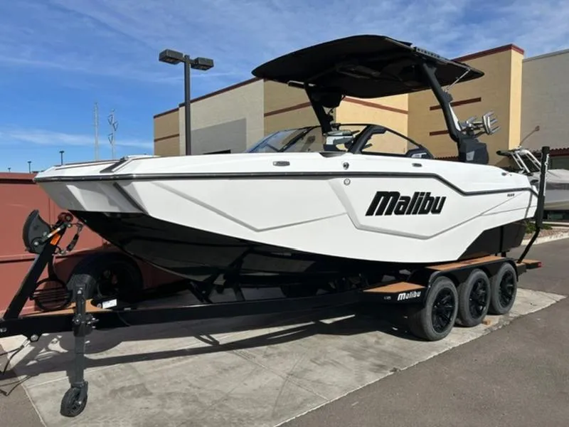 Slide: The Image of 2025 Malibu M230 boat on trailer, white exterior, parked outdoors. - 3