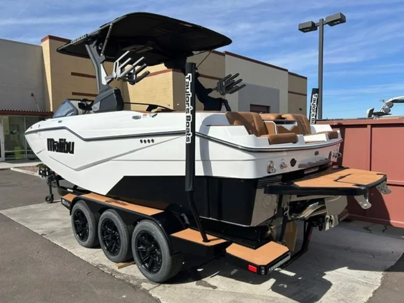 Slide: The Image of 2025 Malibu M230 boat on trailer, white exterior, parked outdoors. - 4