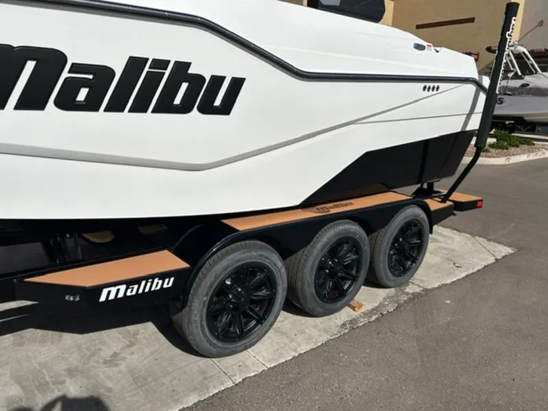 Slide: The Image of 2025 Malibu M230 boat on a triple-axle trailer, featuring sleek design and black wheels. - 5
