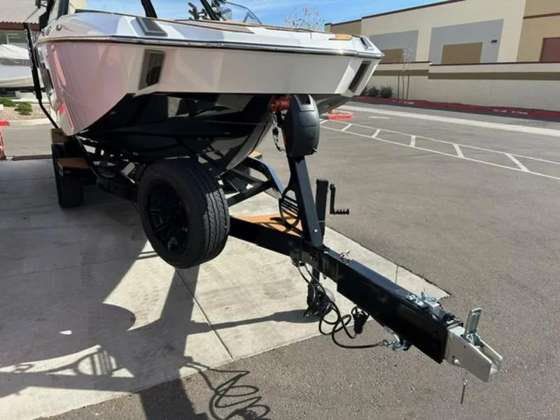 Slide: The Image of 2025 Malibu M230 boat on trailer, parked outdoors in a sunny area. - 7