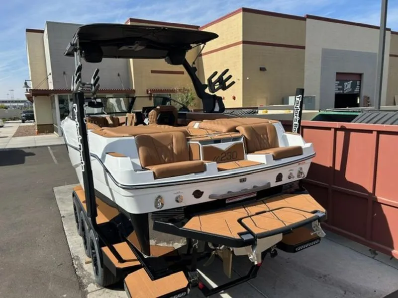 Slide: The Image of 2025 Malibu M230 boat with tan seats, parked outdoors on a trailer. - 8