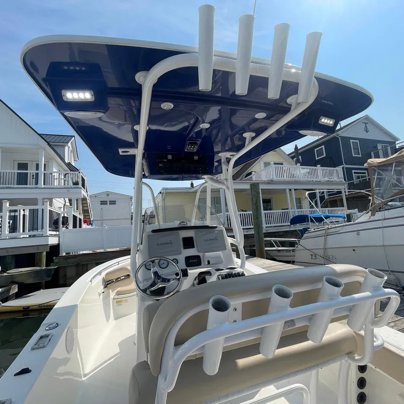 Slide: The Image of 2015 NauticStar 2200XS Offshore boat with T-top and rod holders, docked near houses. - 18