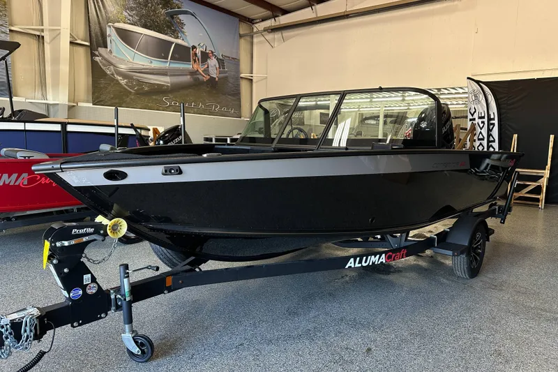 Slide: The Image of 2026 Alumacraft Competitor 185X Sport boat interior with open storage compartments in a showroom. - 8