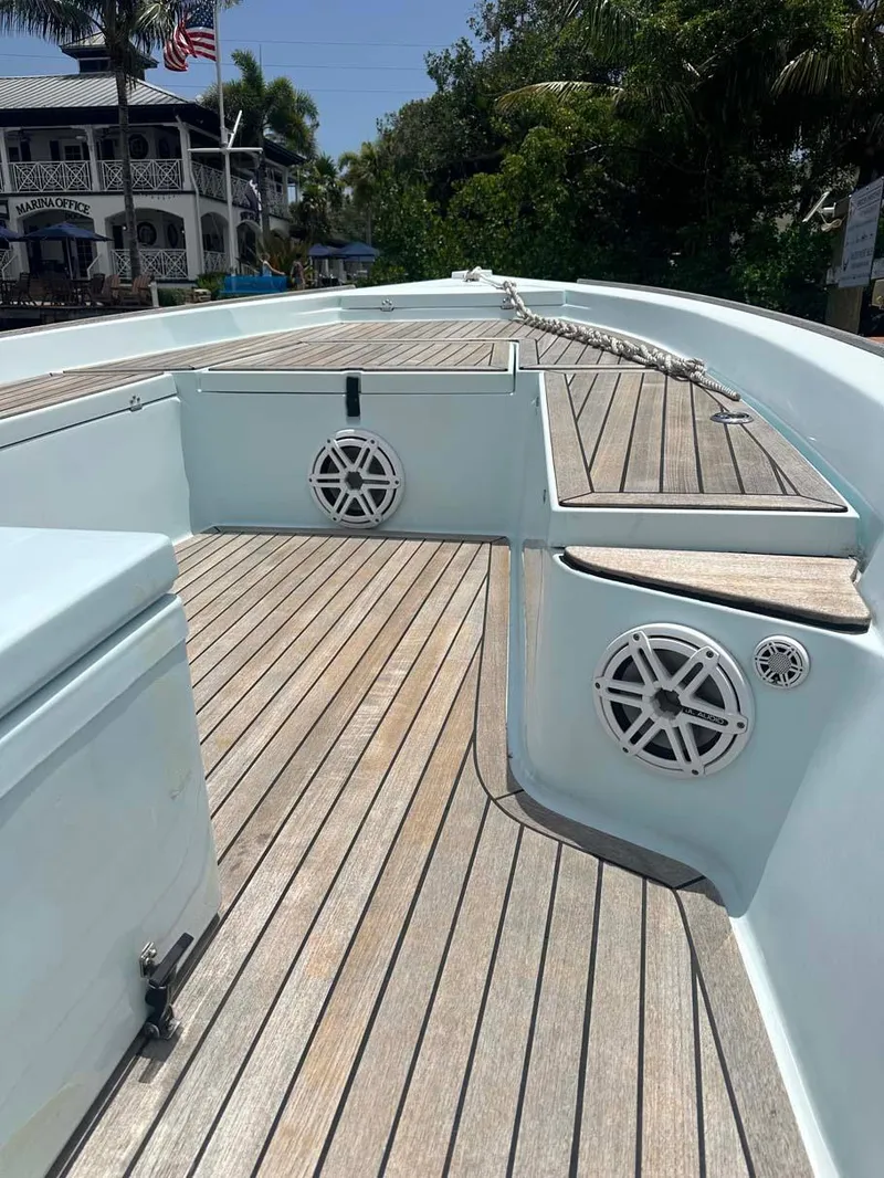 Slide: The Image of 2004 Pathfinder 2400 V boat deck with wooden flooring and speakers, docked near lush greenery. - 6