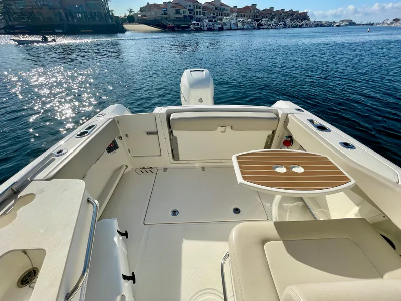 Slide: The Image of 2018 Boston Whaler 230 Vantage boat interior with seating and table, docked by waterfront homes. - 12