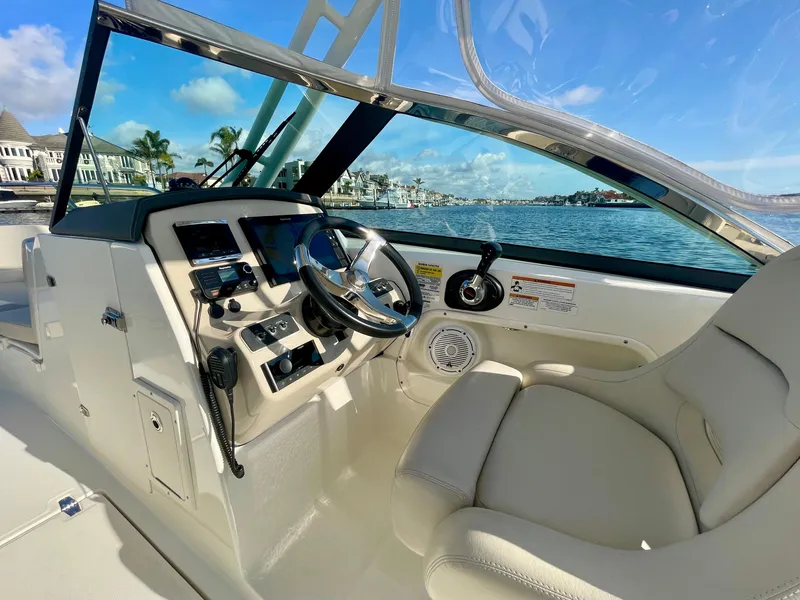 Slide: The Image of 2018 Boston Whaler 230 Vantage boat interior with steering wheel and controls, docked by waterfront homes. - 25