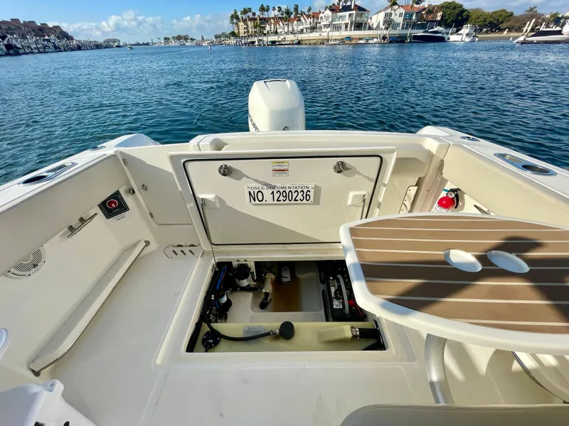 Slide: The Image of 2018 Boston Whaler 230 Vantage boat interior with open storage compartment, docked in a scenic marina. - 46