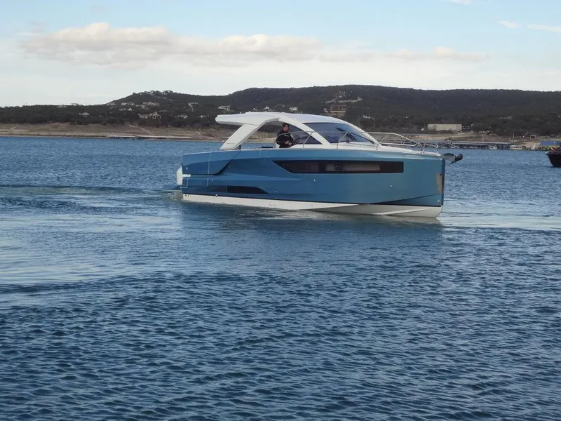 Slide: The Image of 2025 Jeanneau DB/43 OB boat cruising on a calm lake with hills in the background. - 14