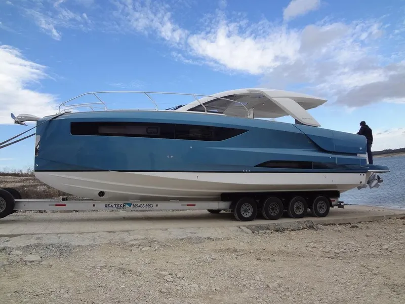 Slide: The Image of 2025 Jeanneau DB/43 OB boat on trailer by the water under a cloudy sky. - 18