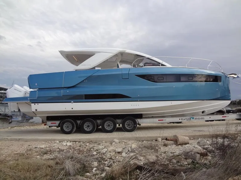 Slide: The Image of 2025 Jeanneau DB/43 OB boat on trailer, blue and white design, parked outdoors. - 24