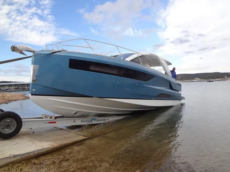 Slide: The Image of 2025 Jeanneau DB/43 OB boat on trailer by the water, under a partly cloudy sky. - 27