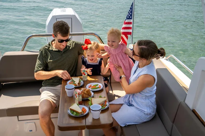 Slide: The Image of Family enjoying a meal on a 2025 Nimbus Weekender 9 boat, with an American flag. - 16