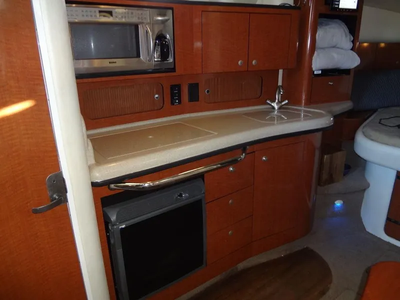 Slide: The Image of 2005 Sea Ray 320 Sundancer interior kitchen with microwave, sink, and wooden cabinetry. - 29