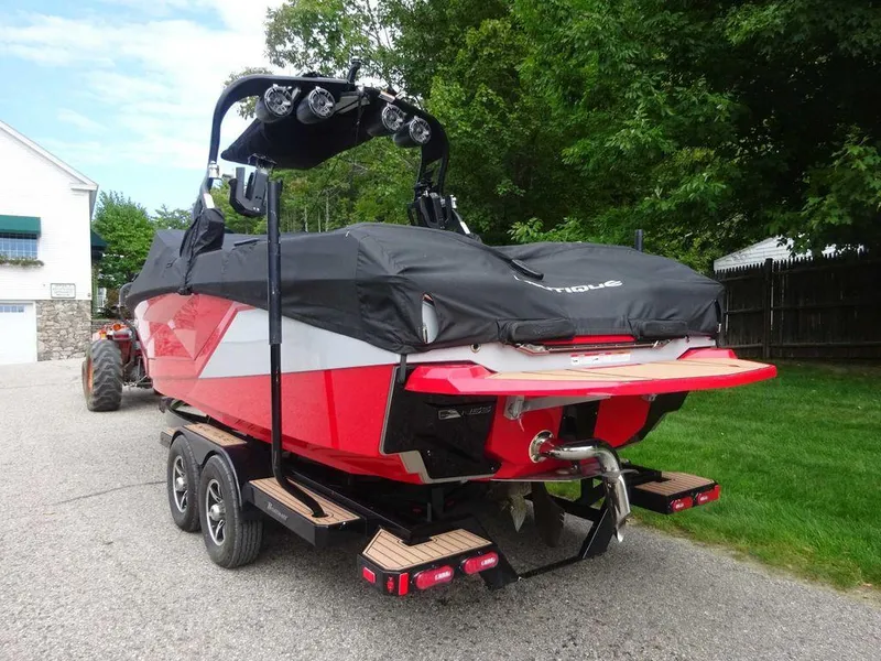 Slide: The Image of 2021 Nautique G23 boat on trailer, covered, red and black design, parked outdoors. - 3