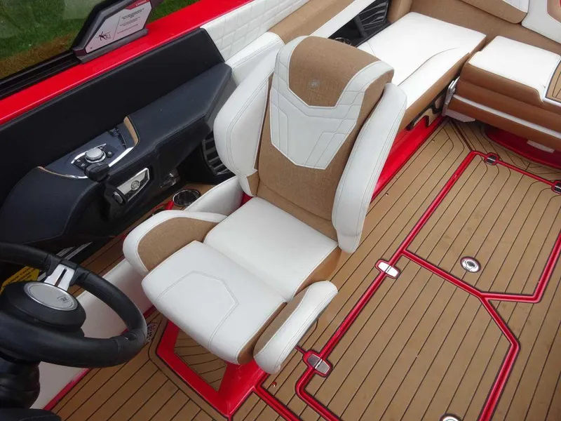Slide: The Image of 2021 Nautique G23 interior with tan and white seating, red accents, and wood-style flooring. - 8