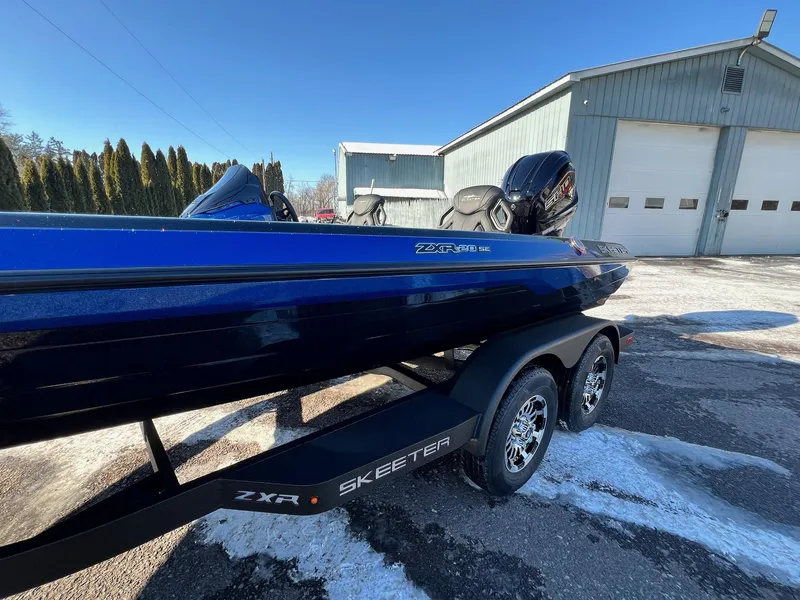 Slide: The Image of 2025 Skeeter ZXR 20 SE boat on trailer, parked outside a large garage. - 16