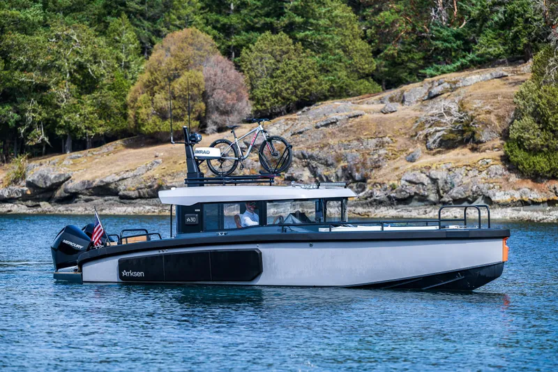 Slide: The Image of 2023 Arksen 30 boat cruising on a scenic lake with a bicycle on the roof. - 5