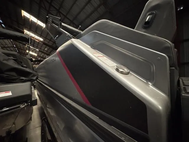 Slide: The Image of 2023 Manitou Explore 22 Max Bench boat, sleek design with red accents, stored indoors. - 24